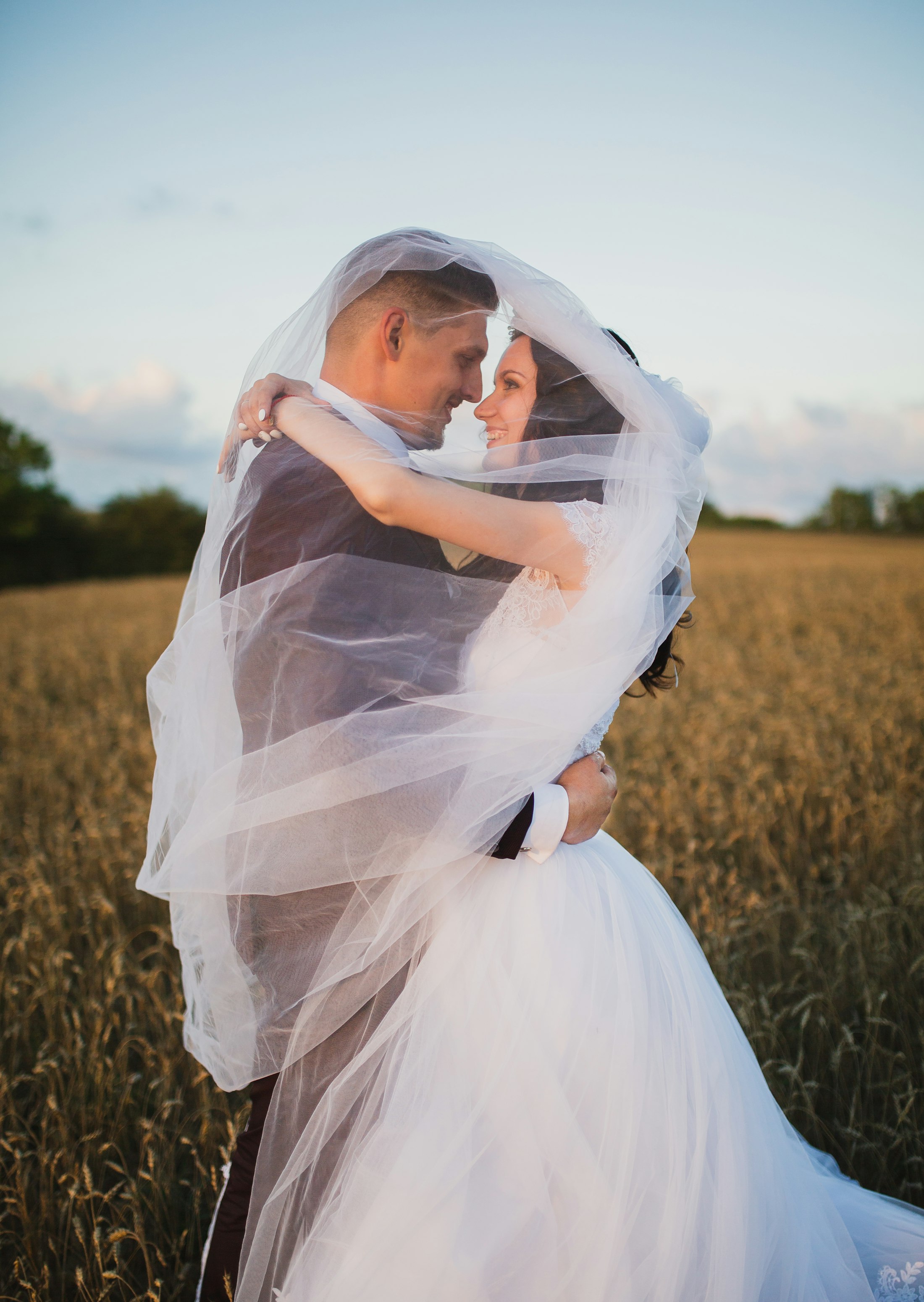 Bride and groom wrapped in a veil in a golden Northern BC field at sunset