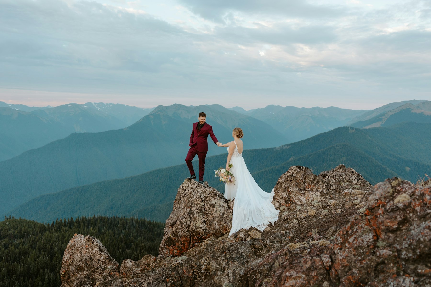 Bride and groom standing on a mountain peak at sunset
