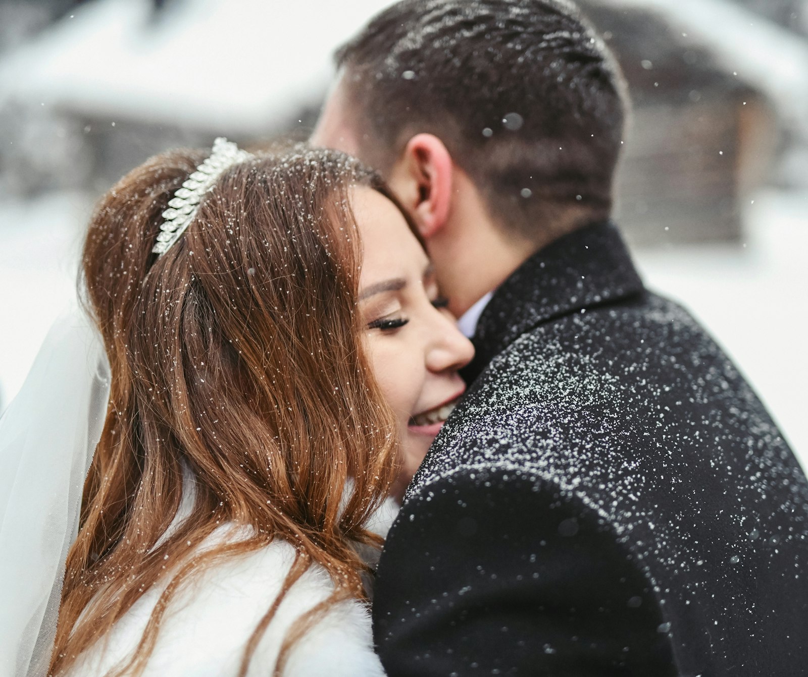 Bride and groom embracing as snow falls on a winter wedding day